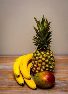 Vertical shot of mango, pineapple and bananas on the wooden surface Fotos de archivo