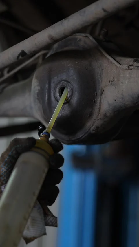 Vertical shot of mechanic pumping fresh fluid into differential gearbox. Stock Footage 344231731