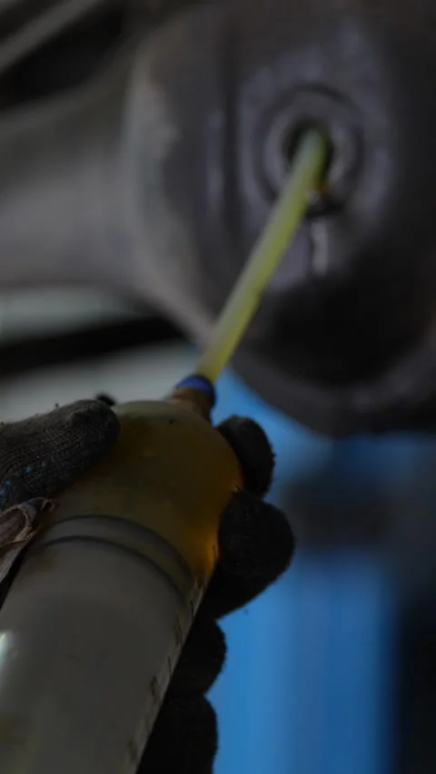 Vertical shot of mechanic pumping fresh fluid into differential gearbox. Stock Footage 344232026
