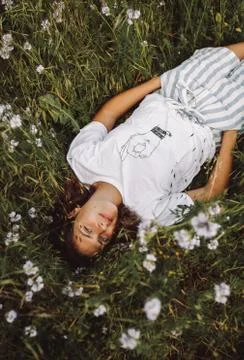 A vertical shot of a model laying down in a daisy field wearing a white graph Stock Photos