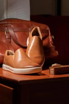 Vertical shot of a pair of brown solid slip shoes before a leather bag over the Fotos Stock