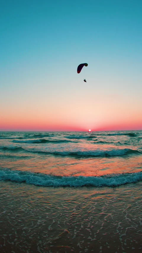 Vertical shot. paraglider flies over the beach. paraglider flies at sunset. Stock Footage 281149828