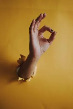A vertical shot of a person's hand breaking through a yellow paper wall showi Stock Photos