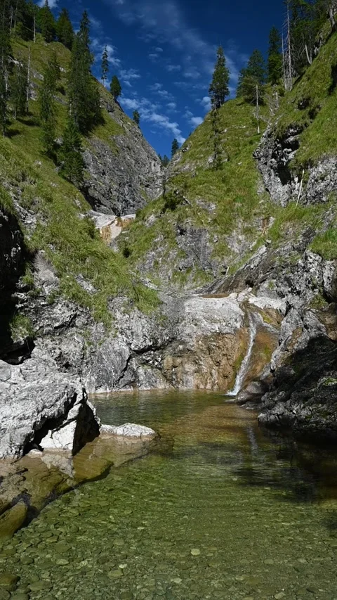 Vertical shot of a pond from a mountain stream and waterfalls in the background Video stock 260894126