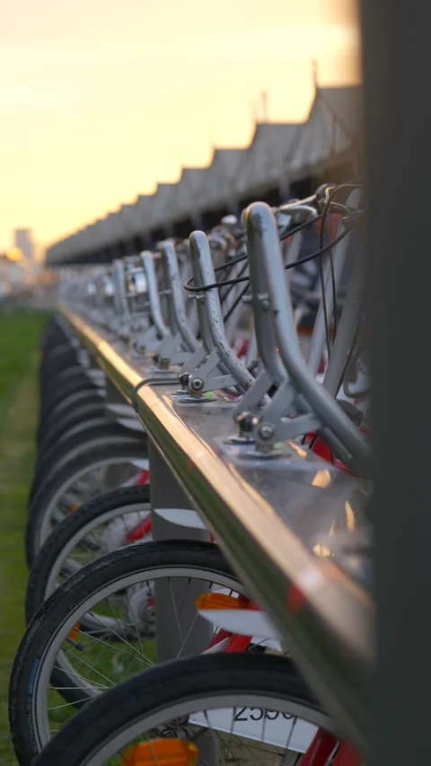 Vertical shot of rack of red sharing bikes in city at golden hour Видео 222071400