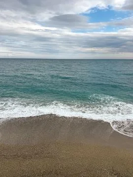 Vertical shot of sea waves hitting pebble shore with soft cloudy sky Stock Photos