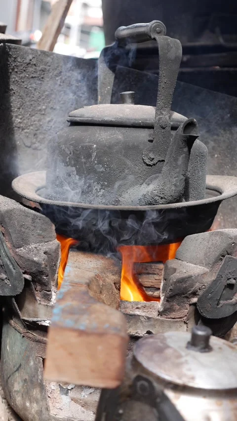 A vertical shot shows a blackened kettle standing over fire inside a clay stove 스톡 동영상 341408526