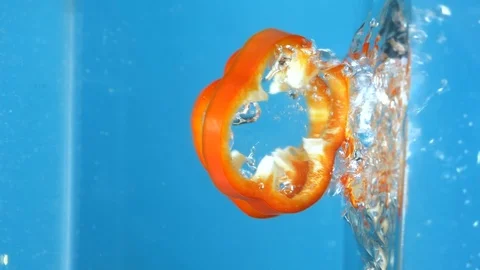 Vertical shot. sliced red bell peppers fall into the water. blue background Stock Footage 126603258