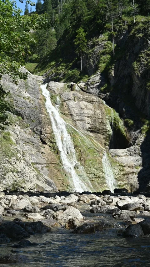 Vertical shot of a stoney mountain stream in front of a slow moving waterfall Video stock 260891593