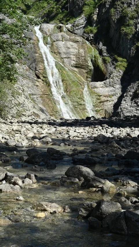 Vertical shot of a stoney mountain stream in front of a slow moving waterfall Stock-Footage 260891742