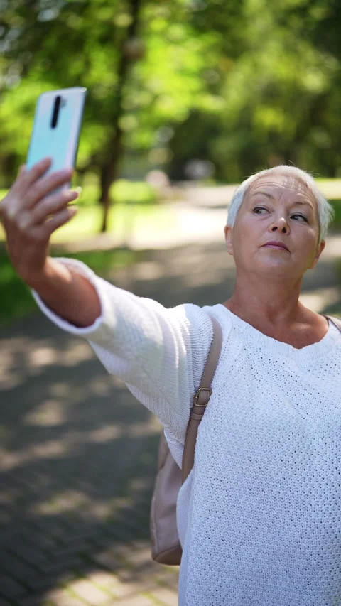 Vertical shot of stylish gray-haired senior woman taking selfie using mobile Stock Footage 287345396