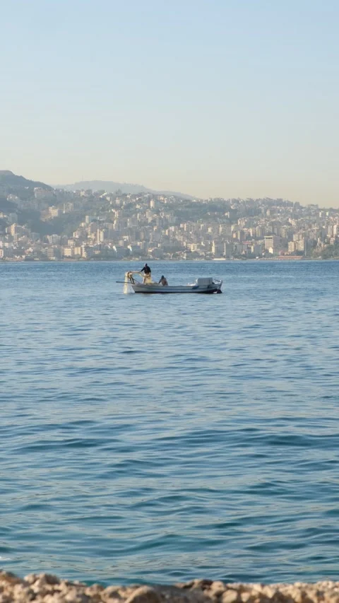 Vertical shot of Two Fishermen in a Small Boat Removing Fishnets from the Sea Stock Footage 288976327