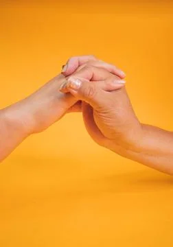 Vertical shot of two hands holding each other on a yellow background Stock Photos