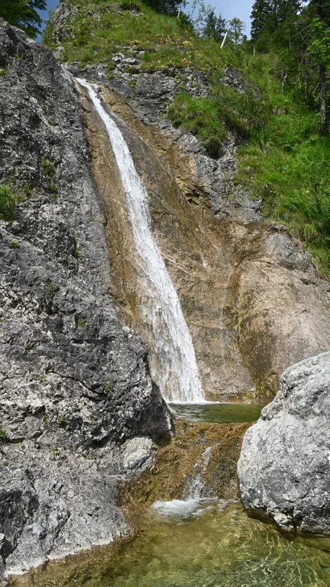 Vertical shot of a waterfall next to a steep meadow in the mountains 스톡 동영상 260885916