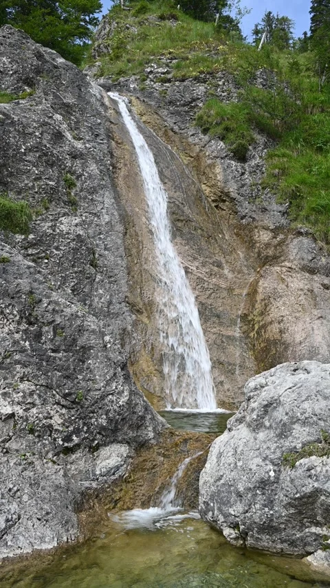 Vertical shot of a waterfall next to a steep meadow in the mountains, overcast Stock Footage 260886064