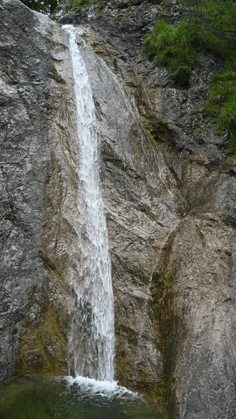 Vertical shot of a waterfall running over rocks into a pond, overcast Stock Footage 260887200