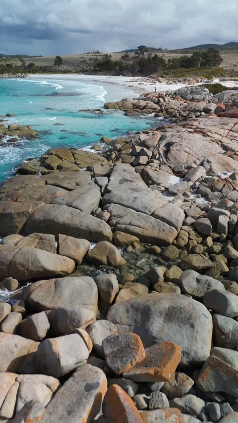 Vertical shot of waves crashing on orange lichen rocks and white sand. Vídeo Stock 332542502
