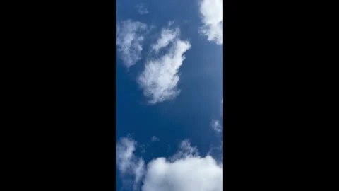 Vertical shot of white clouds drifting across a bright blue sky on a sunny day Stock Footage 344769207