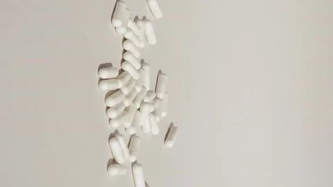 Vertical shot of white pill drop on grey or white surface with capsules.Medicine Stock Footage 229499397