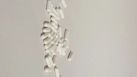 Vertical shot of white pills drop on grey or white surface with capsules. Stock Footage 229499392