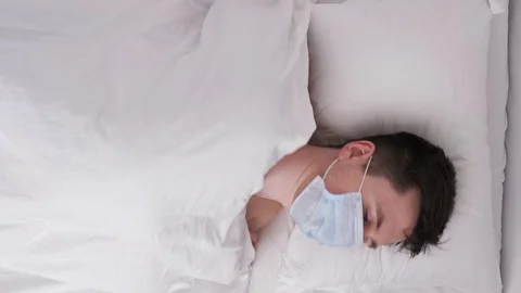 Vertical shot young man lies in bed in medical mask Stock Footage 128731664