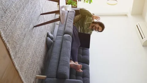 Vertical shot of young man in video call saying goodbye to laptop on the sofa Stock Footage 164905577