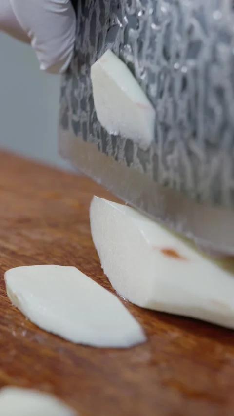 Vertical: Side angle shot of peeled white Chinese yam being sliced into pieces. Stock Footage 341837130