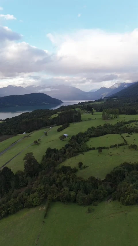 Vertical Side Tracking Over Green Field Towards Cochamó Fjord and Mountains Vídeo Stock 326078581