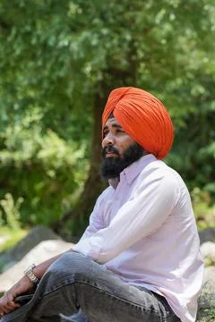 Vertical side view of a Sikh man in an orange turban sitting and looking away. Stock Photos