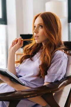 Vertical side view of thoughtful young woman student sitting on cozy chair at Stock Photos