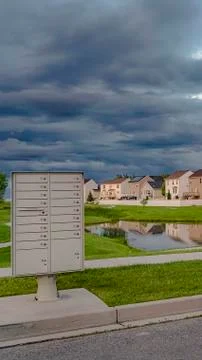 Vertical Sky filled with gray clouds over homes and pond amid a vast grassy Foto stock