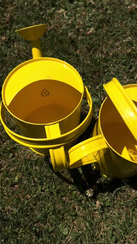 Vertical slow camera movement over two yellow kids watering cans, slow motion Stock Footage 312528692