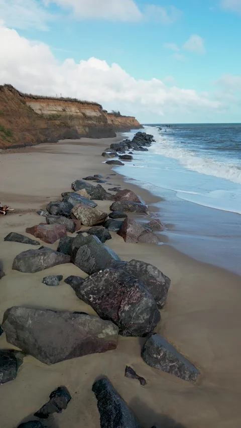 Vertical slow motion boulder strewn rocky beach flyover Video stock 220312301