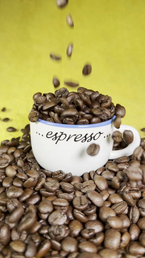 Vertical - Slow motion coffee beans pouring in and around an espresso cup. Video stock 303628759