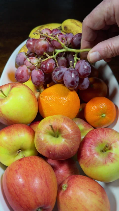 Vertical - Slow motion of a hand placing a grapes on top of a bowl of fruit. Stock Footage 299988383