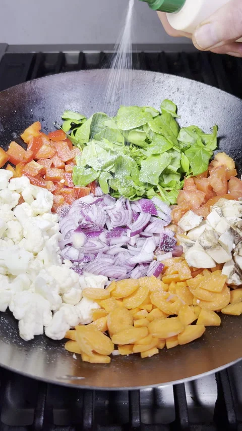 Vertical - Slow motion of a hand spraying oil over raw vegetables in a wok. Stock Footage 303725744