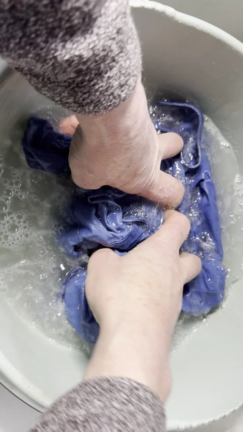 Vertical - Slow motion of a man’s hands squeezing a blue shirt in soapy water. Video stock 300369704