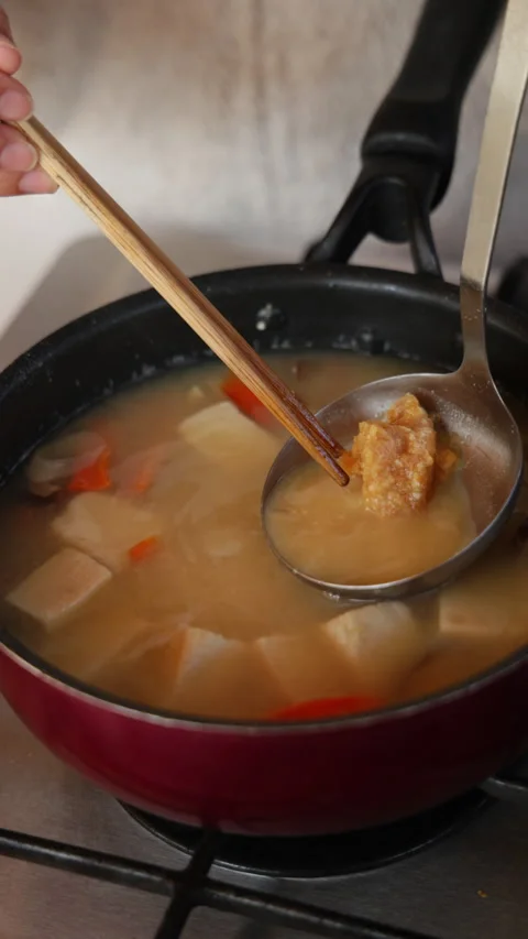 Vertical slow motion miso on a ladle over a pot of vegetable soup Video stock 348196845
