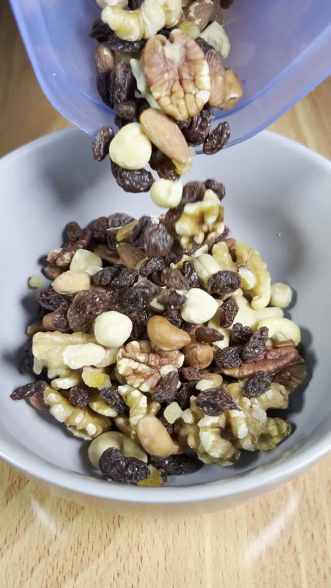 Vertical - Slow motion of mixed shelled nuts and raisins pouring into a bowl. Video stock 300097507