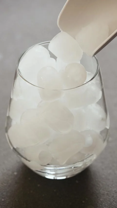 Vertical slow-motion pouring ice cubes into glass cup on kitchen counter Stock Footage 342239266