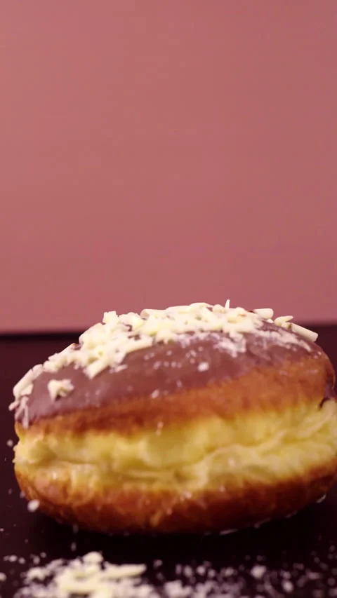 Vertical slow-motion shot of a Berliner donut falling, with white chocolate Stock Footage 297351598