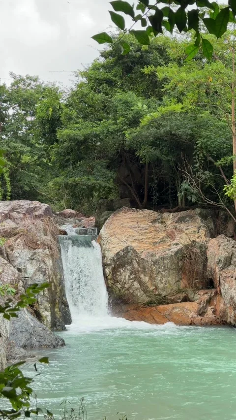 A vertical slow motion shot captures a waterfall feeding a small lagoon-like Stock Footage 324853520
