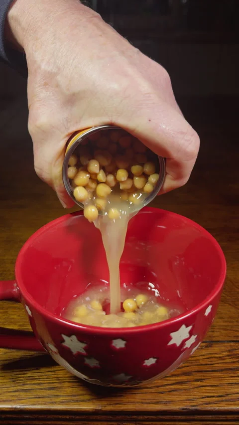 Vertical - Slow motion shot of a hand pouring chick peas from a can into a bowl. Stock Footage 295205682