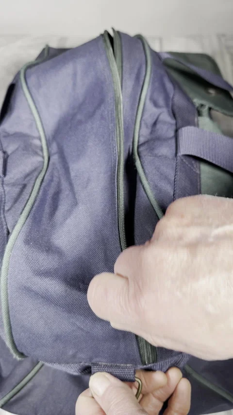 Vertical - Slow motion shot of a senior man’s hands unzipping a travel bag. Video stock 304086569