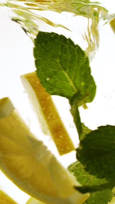 Vertical slow motion slices of lemon fruit and mint leaves splashing in water Stock Footage 266483388