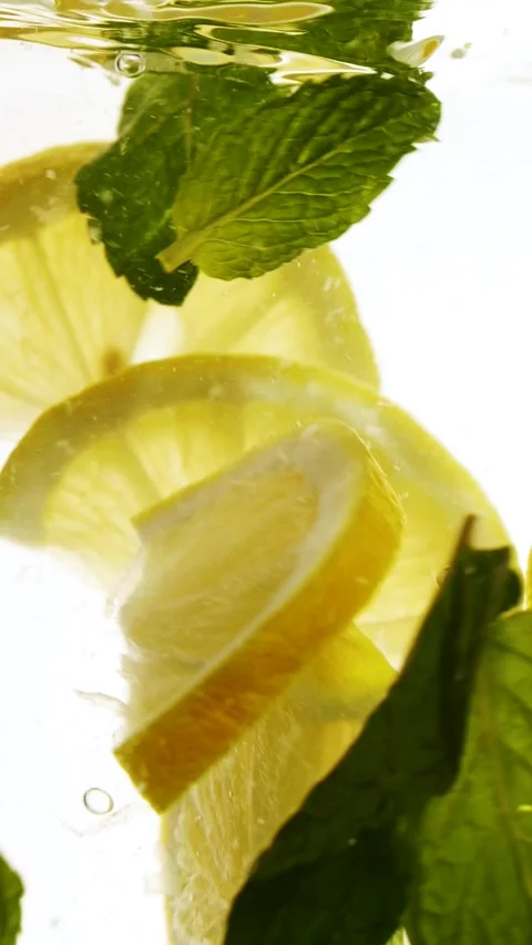 Vertical slow motion slices of lemon fruit and mint leaves splashing in water Stock Footage 270345763