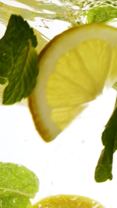 Vertical slow motion slices of lemon fruit and mint leaves splashing in water Stock Footage 271118186