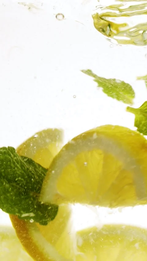 Vertical slow motion slices of lemon fruit and mint leaves splashing in water Stock Footage 272202309