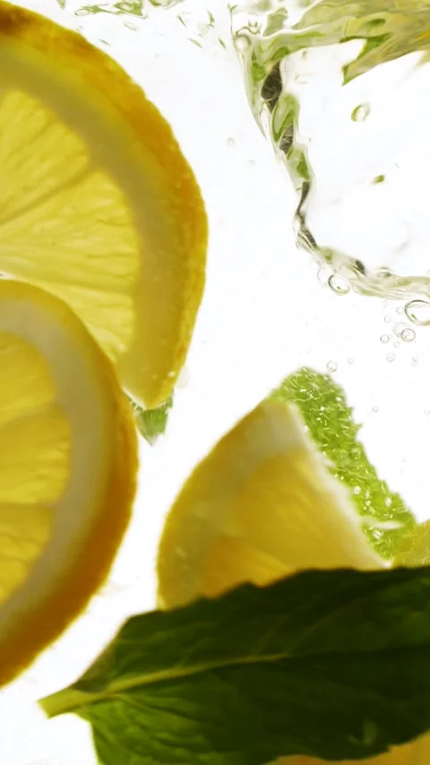 Vertical slow motion slices of lemon fruit and mint leaves splashing in water Stock Footage 273126983
