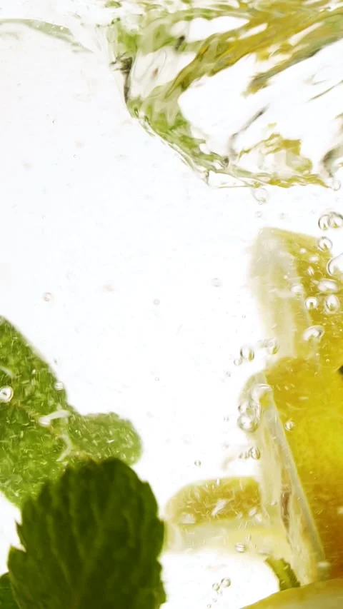 Vertical slow motion slices of lemon fruit and mint leaves splashing in water Stock Footage 273844044